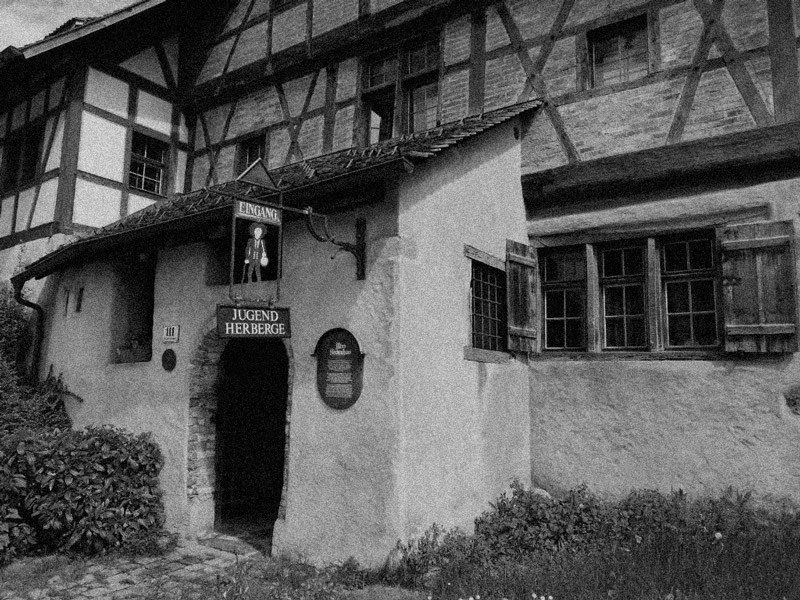 Historisches Hostel in Feldkirch in einem Fachwerkhaus mit kleinem Eingang und Holzfenstern, Schwarz-Weiß-Fotografie.