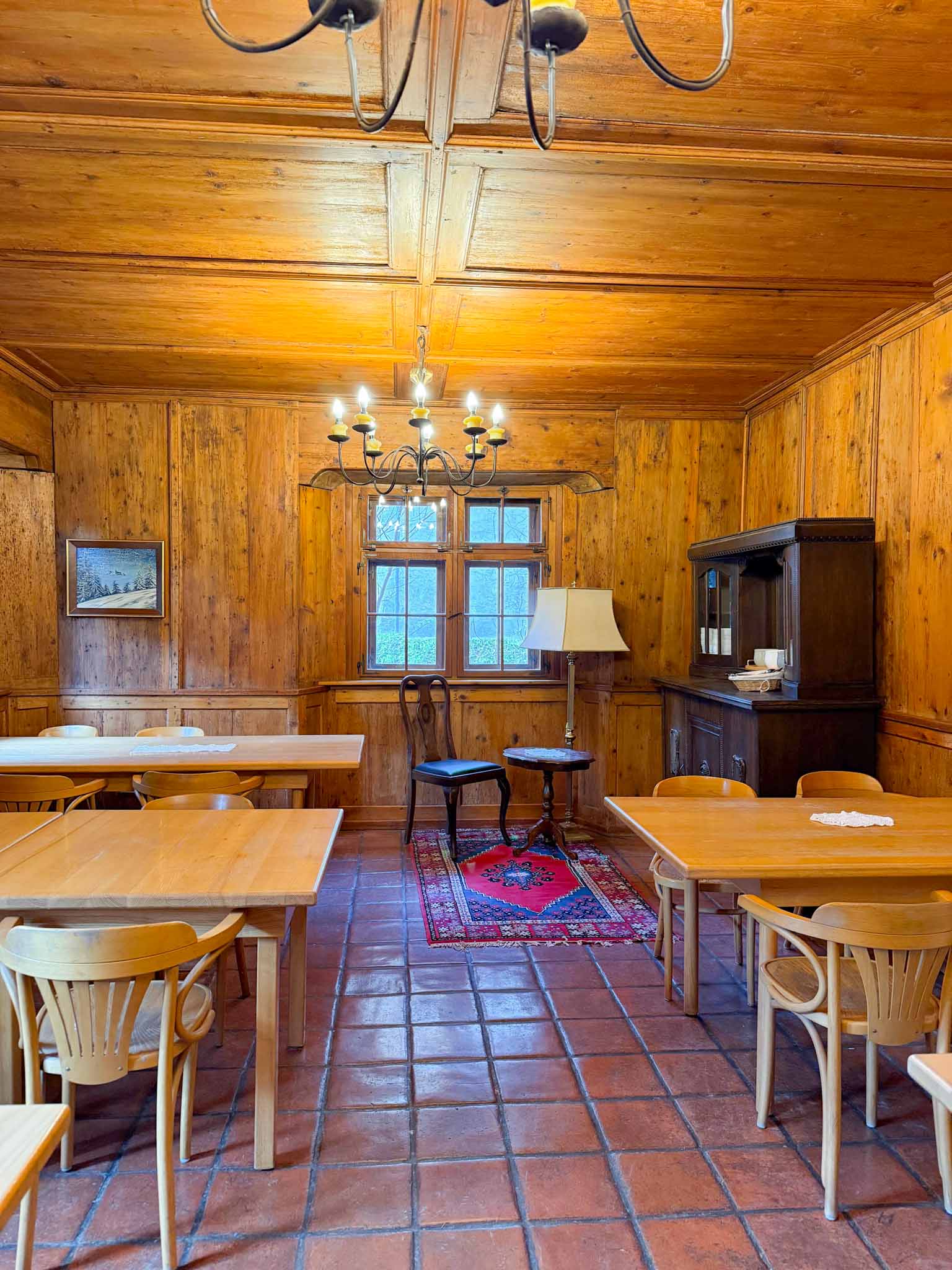 Kleiner Salon im Hostel Feldkirch für bis zu 20 Personen mit Holztischen, Stühlen, mehreren Kronleuchtern, Fenster und gemütlichem Holzambiente.